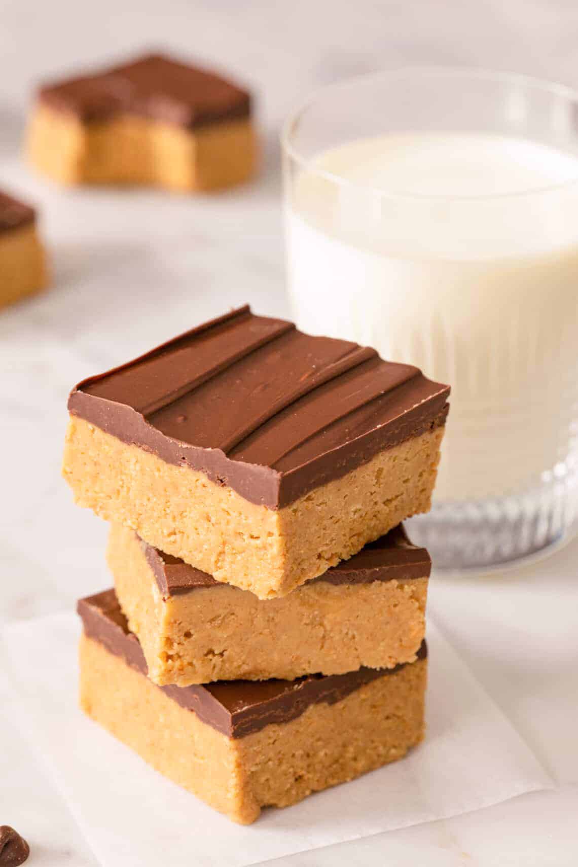 A stack of peanut butter bars on a marble surface alongside a glass of milk.