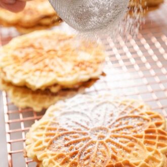 A pinterest graphic of powdered sugar dusted over pizzelle cookies on a cooling rack.