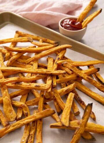 A pile of sweet potato fries on a golden baking sheet.