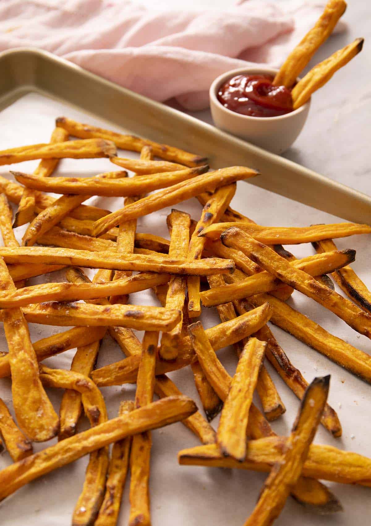 A pile of sweet potato fries on a golden baking sheet.