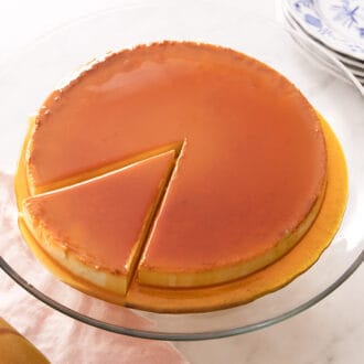 A glass dish with a flan with a slice cut.