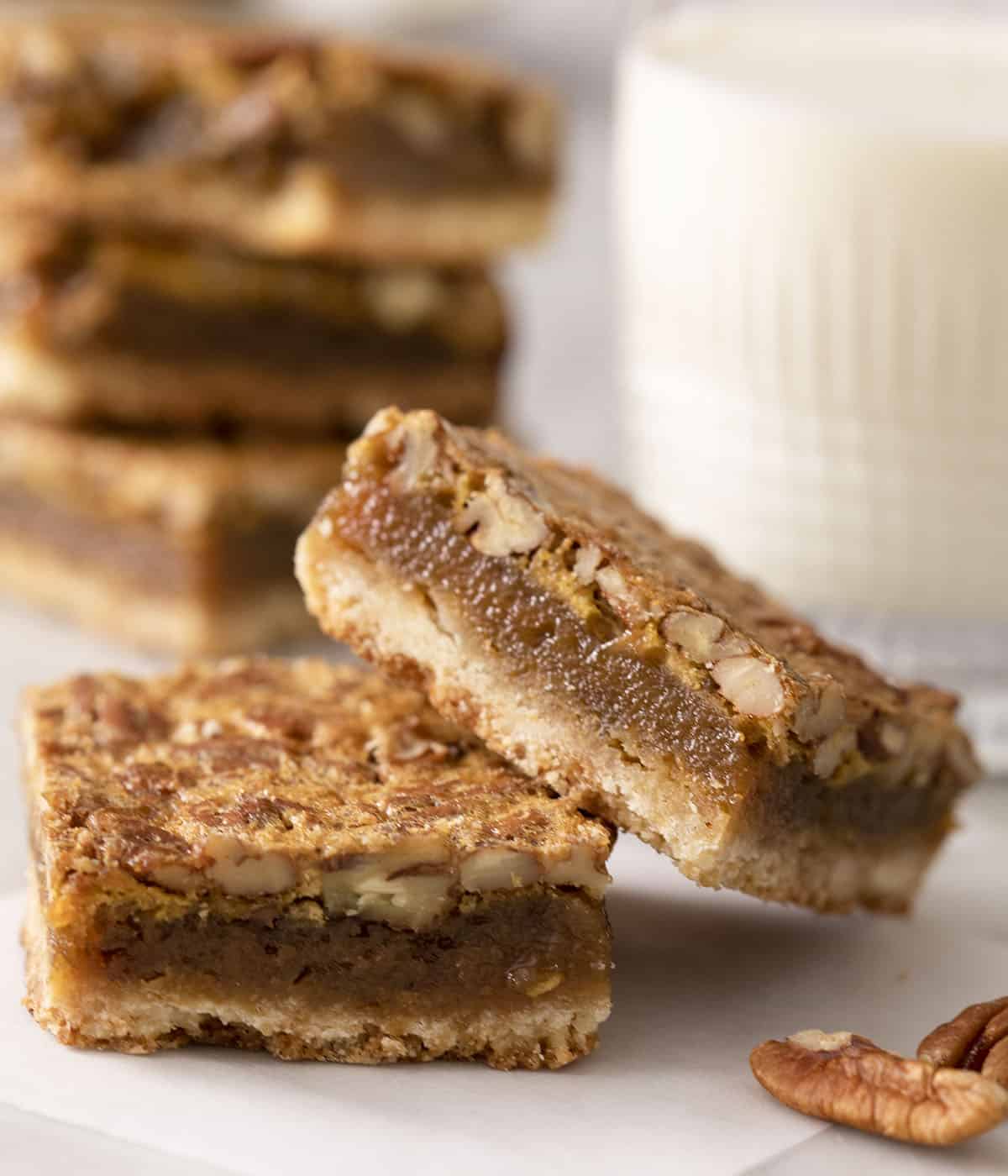 Two pecan pie bars on a marble counter next to a glass of milk.
