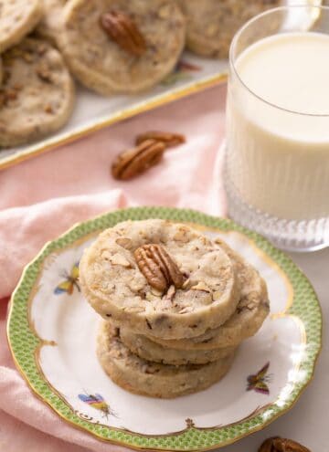 A stack of pecan sandies on a plate next to a glass of milk.