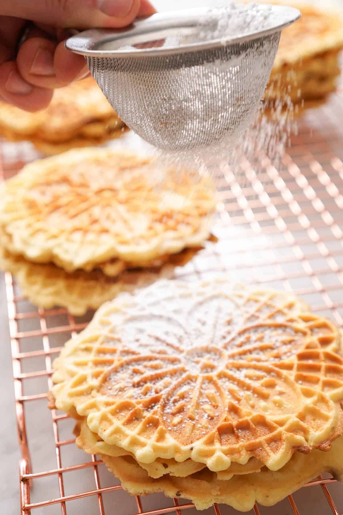 Powdered sugar getting dusted over pizzelle cookies.