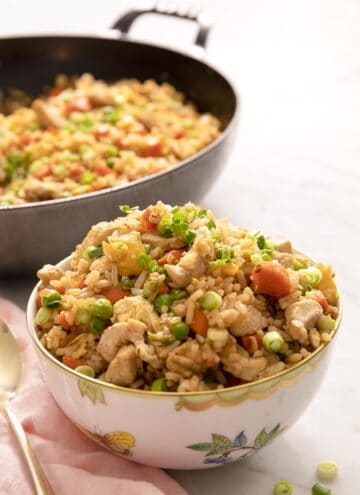 Chicken fried rice in a white bowl with a skillet behind it