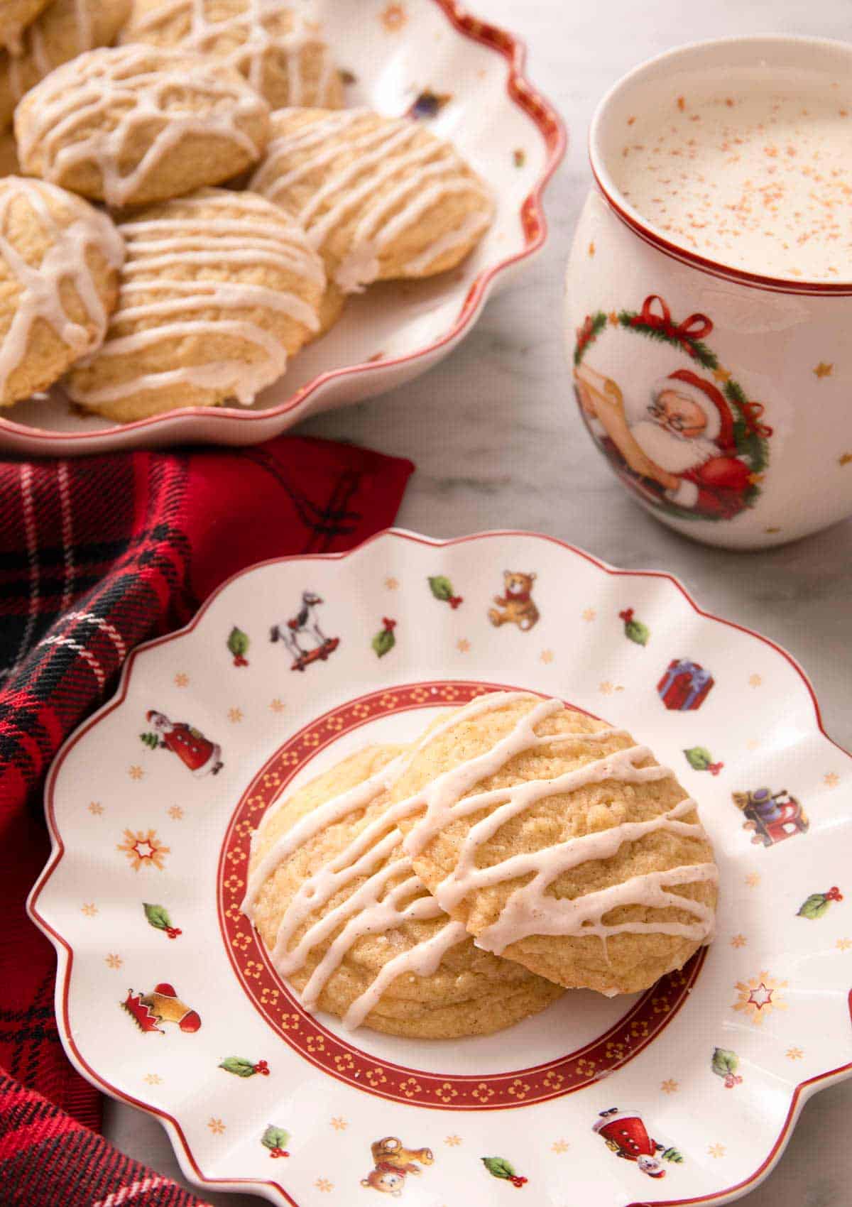 Eggnog cookies on a plate with a mug of hot cocoa behind it
