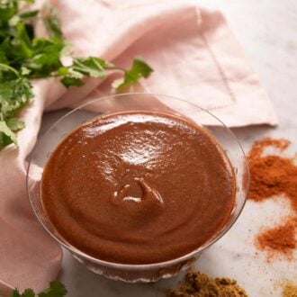 Pinterest graphic showing enchilada sauce in a small glass bowl with cilantro and spices around it.