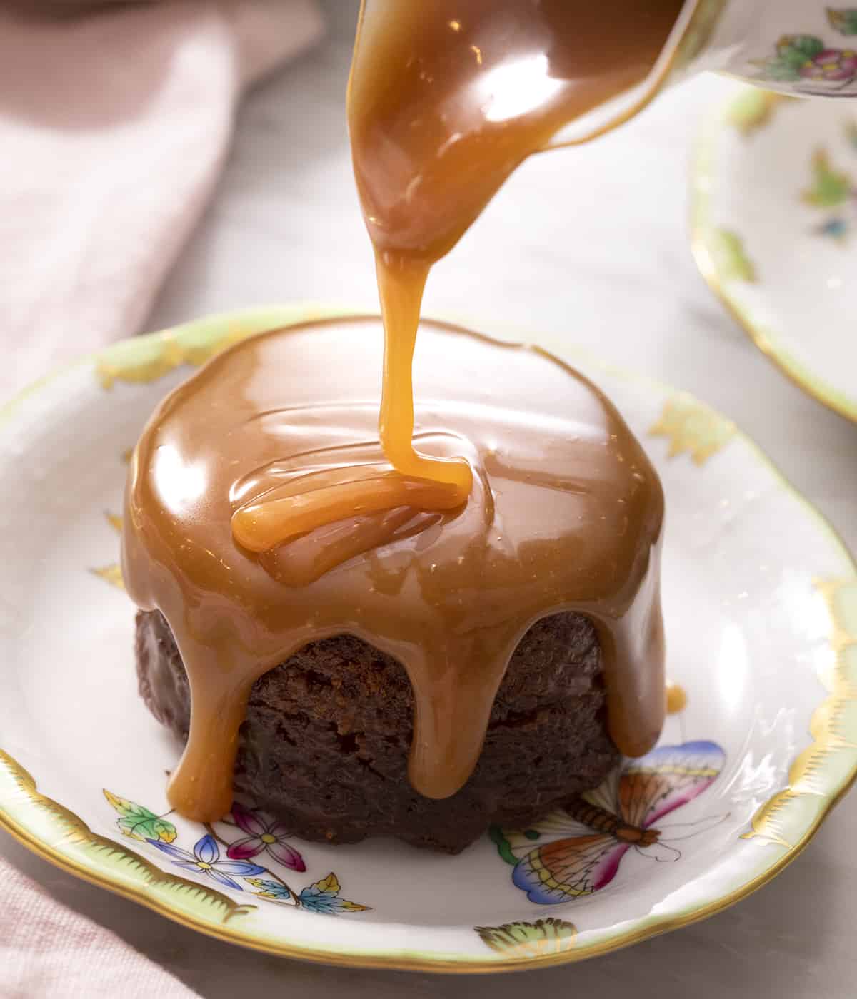A close up of toffee sauce getting poured over a sticky toffee puddng