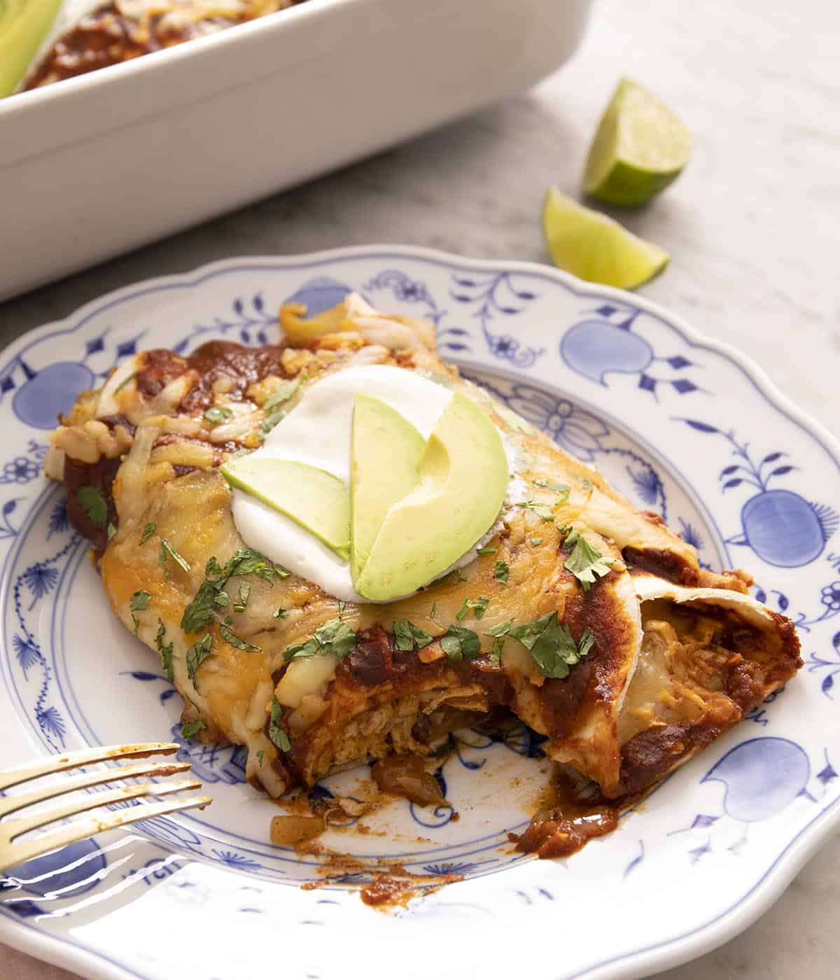 Chicken enchiladas on a plate topped with sour cream and avocado.