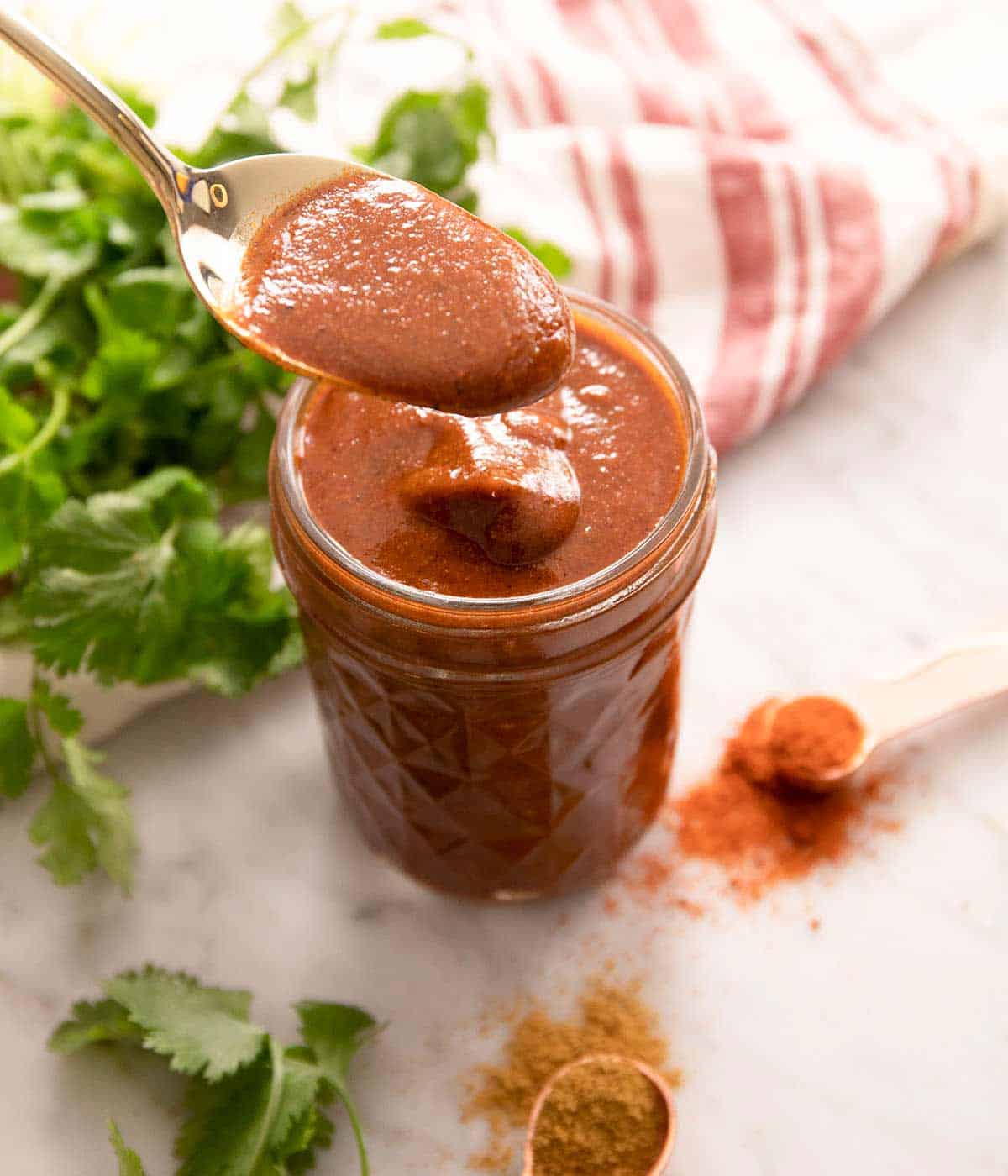 A spoon scooping some enchilada sauce out of a jar