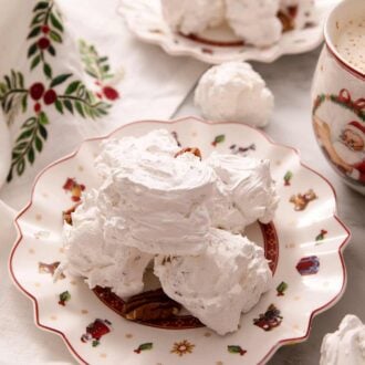A close up of three pieces of divinity candy on a plate. A mug of hot chocolate and more candy in the background.