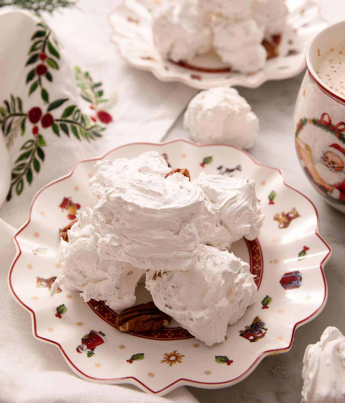 A plate with a stack of divinity candy with pecans. A mug of hot chocolate and more candy in the background.