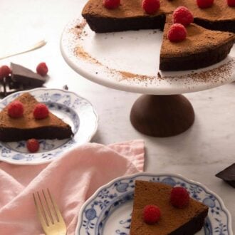 A pinterest graphic of two slices of flourless chocolate cake on plates with the rest of the cake in the background.