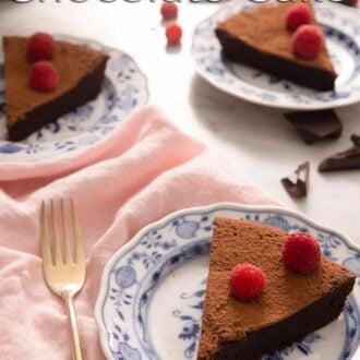 A pinterest graphic of a slice of flourless chocolate cake on a plate topped with raspberries. More slices in the background.
