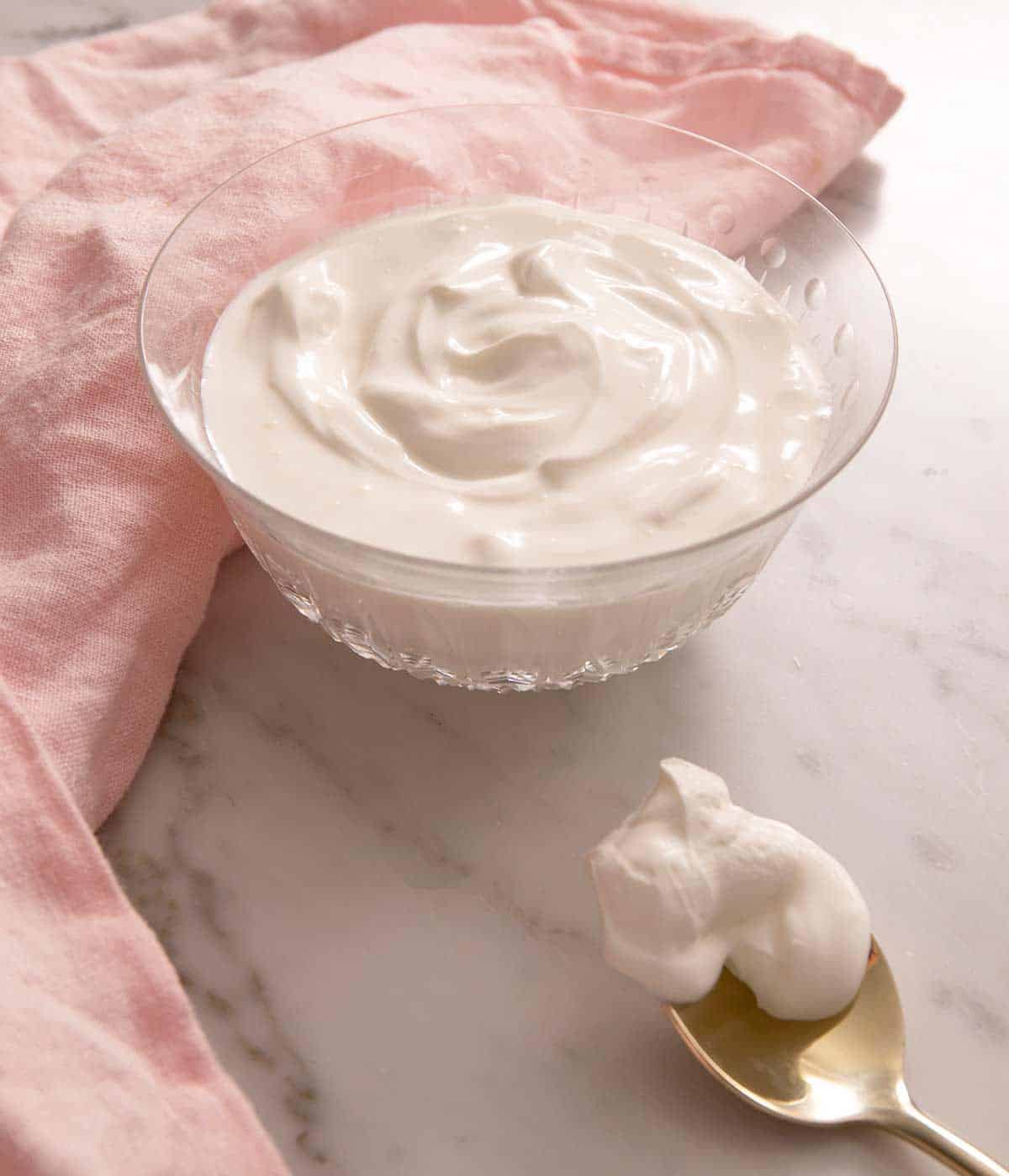 A bowl of homemade sour cream sitting on a marble work surface with a spoonful next to it.
