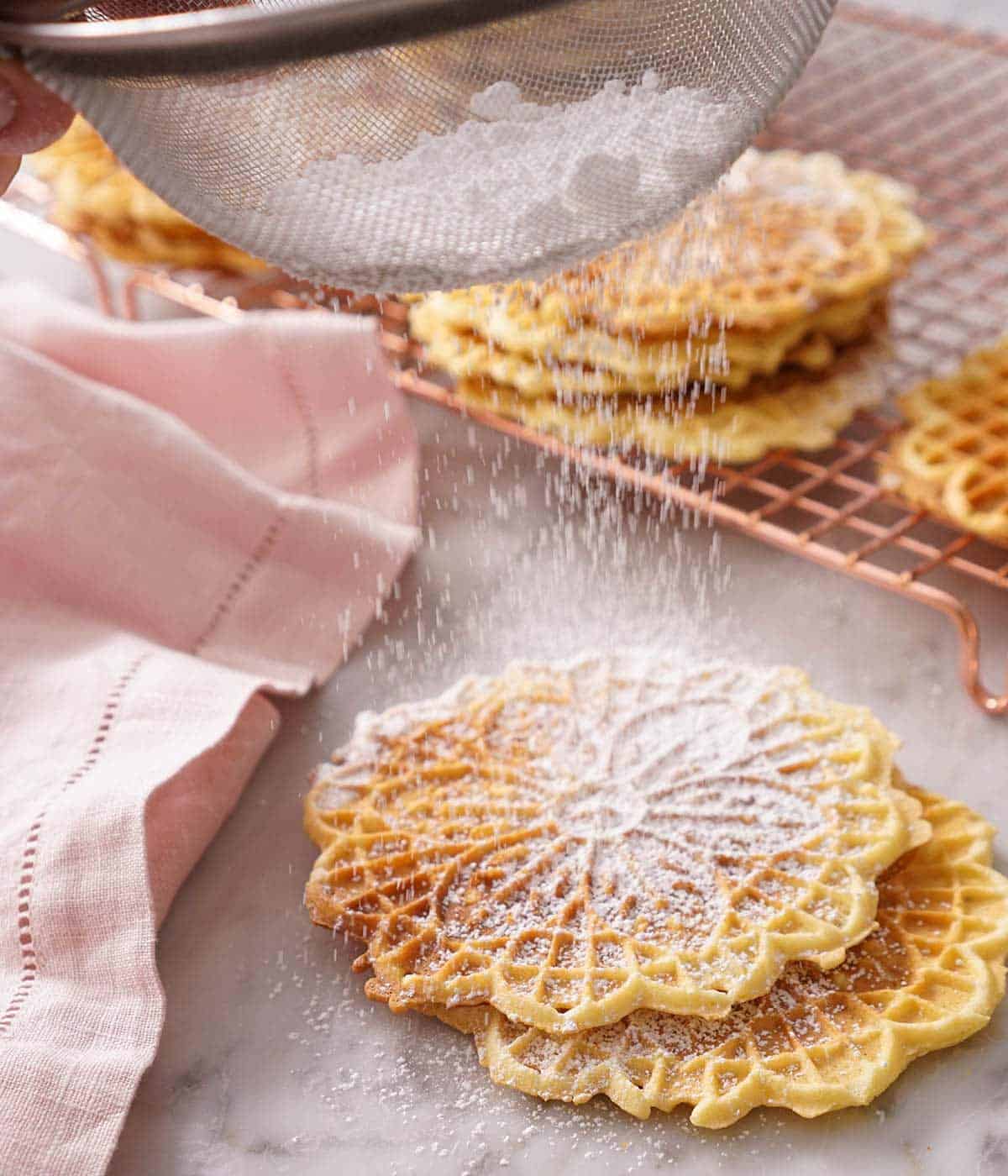 Powdered sugar getting dusted on Pizzelle cookies