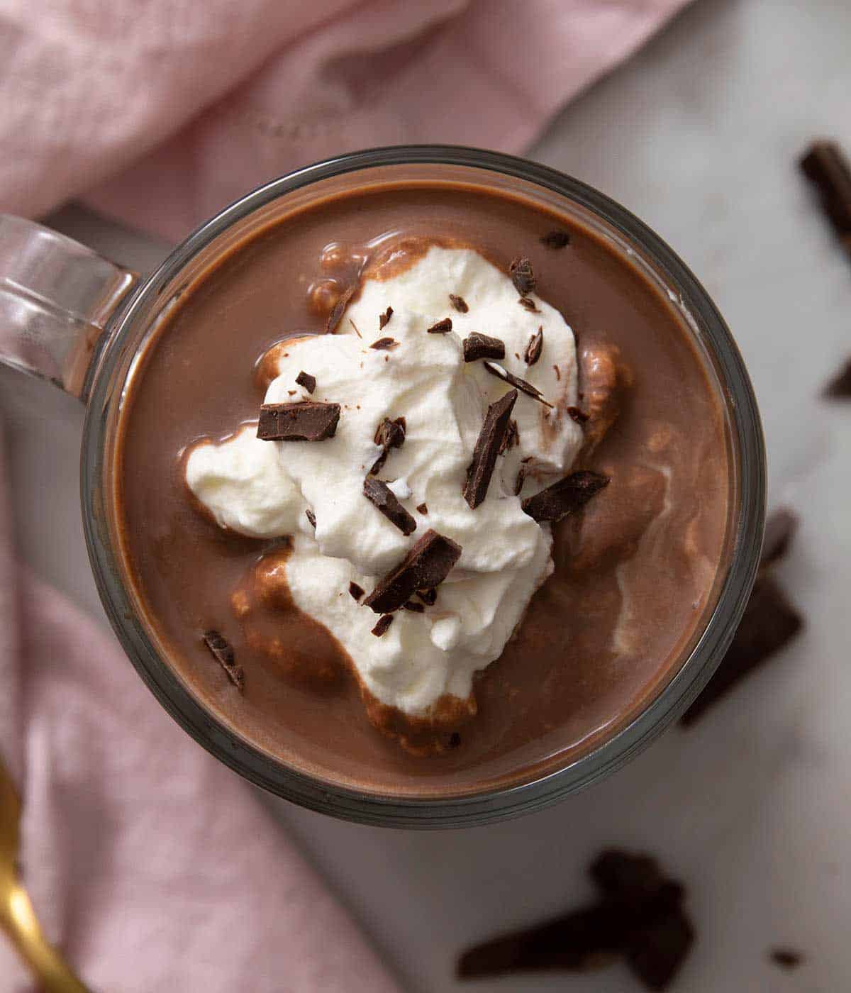 An overhead shot of a mug of hot chocolate topped with whipped cream and shaved chocolate.