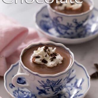 A pinterest graphic of two cups of hot chocolate topped with whipped cream and chocolate.