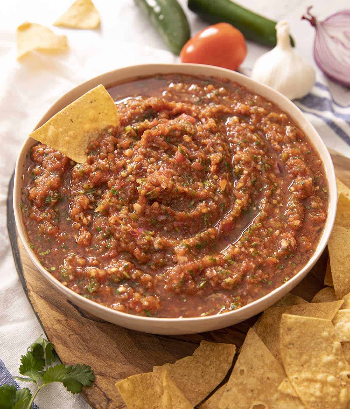 Salsa in a bowl with a tortilla chip at the side and one tucked into the salsa. 