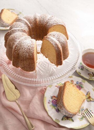 Sour cream pound cake on a cake stand with a slice on a plate.