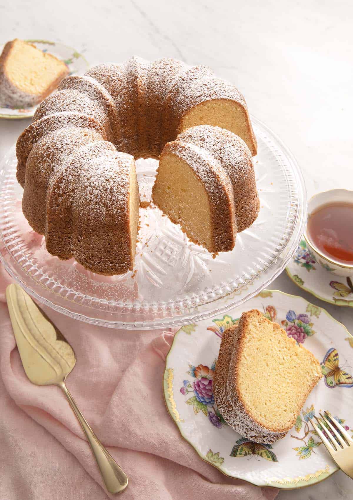 Sour cream pound cake on a cake stand with a slice on a plate.