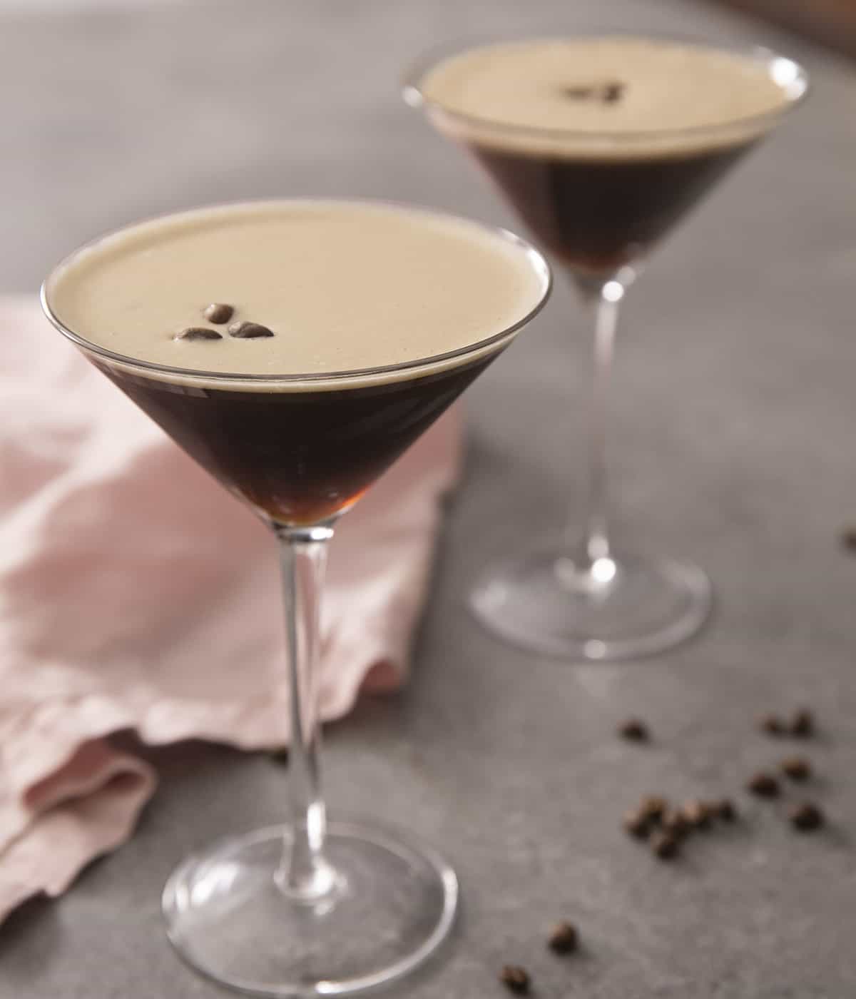 Two espresso martinis in martini glasses topped with coffee beans.