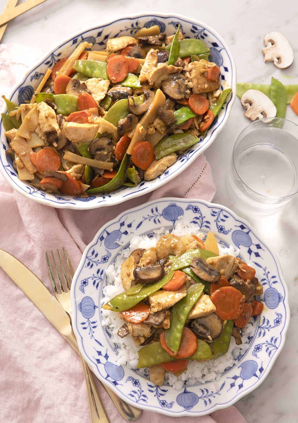 An overhead shot of moo goo gai pan in a platter and some served over a plate of rice.