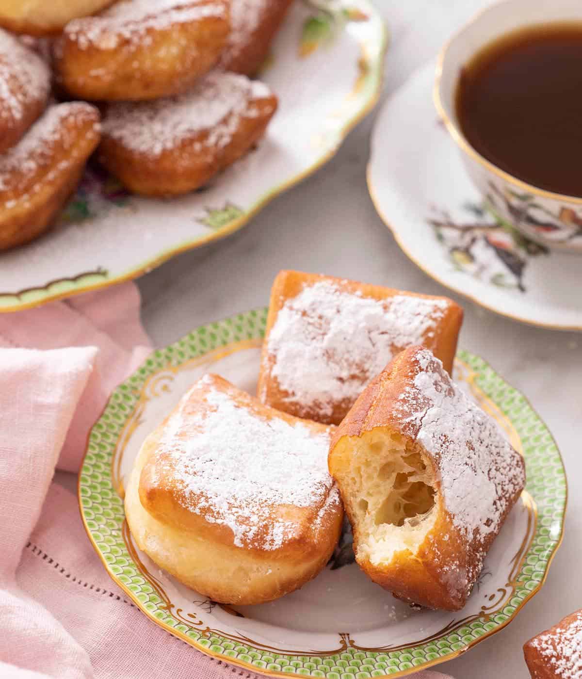 Three beignets on a plate with a cup of tea on the side.