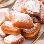 A pile of Beignets on a platter with icing sugar on top.