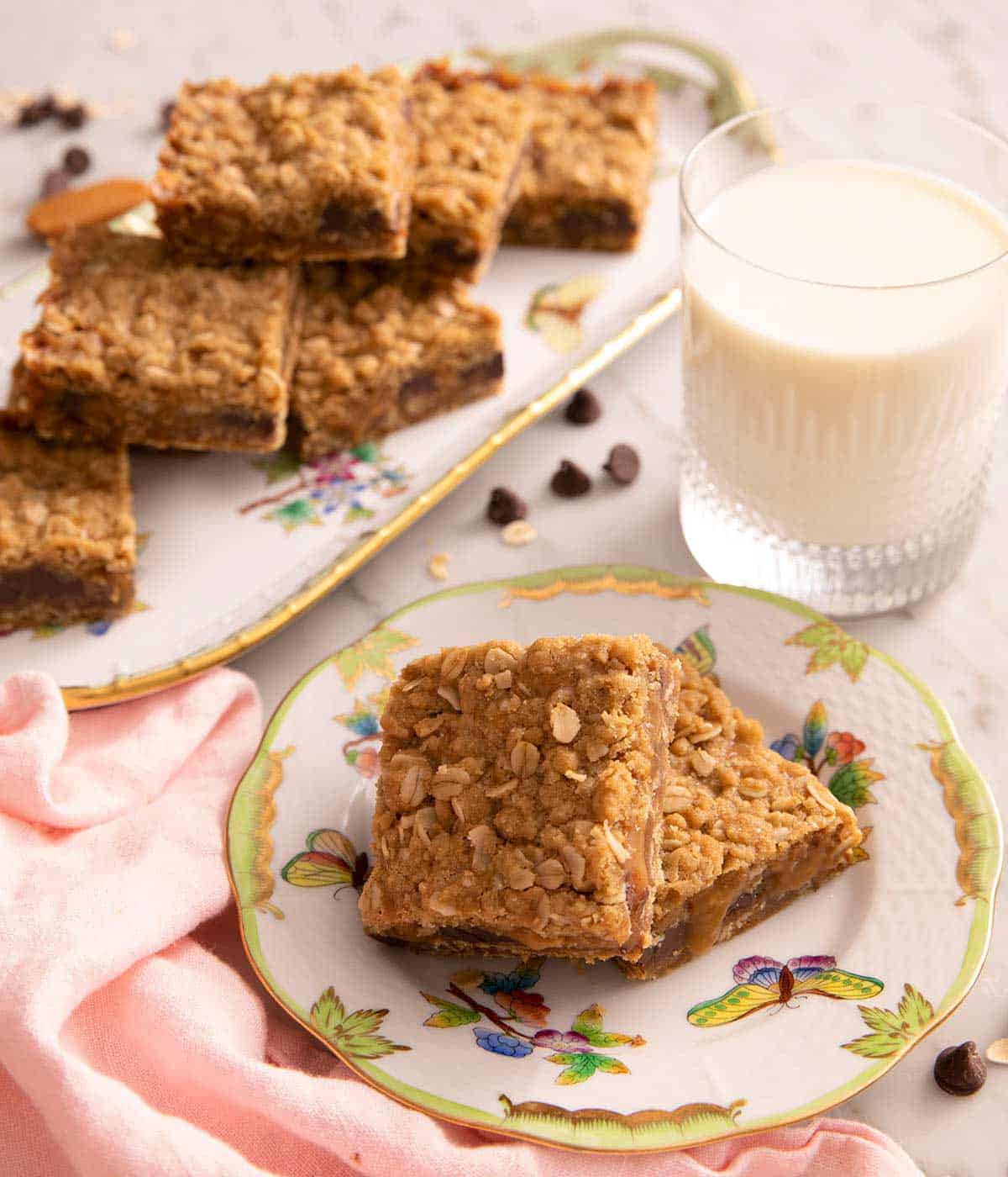 Two Carmelitas on a small plate with a glass of milk at the side with a platter in the back. 