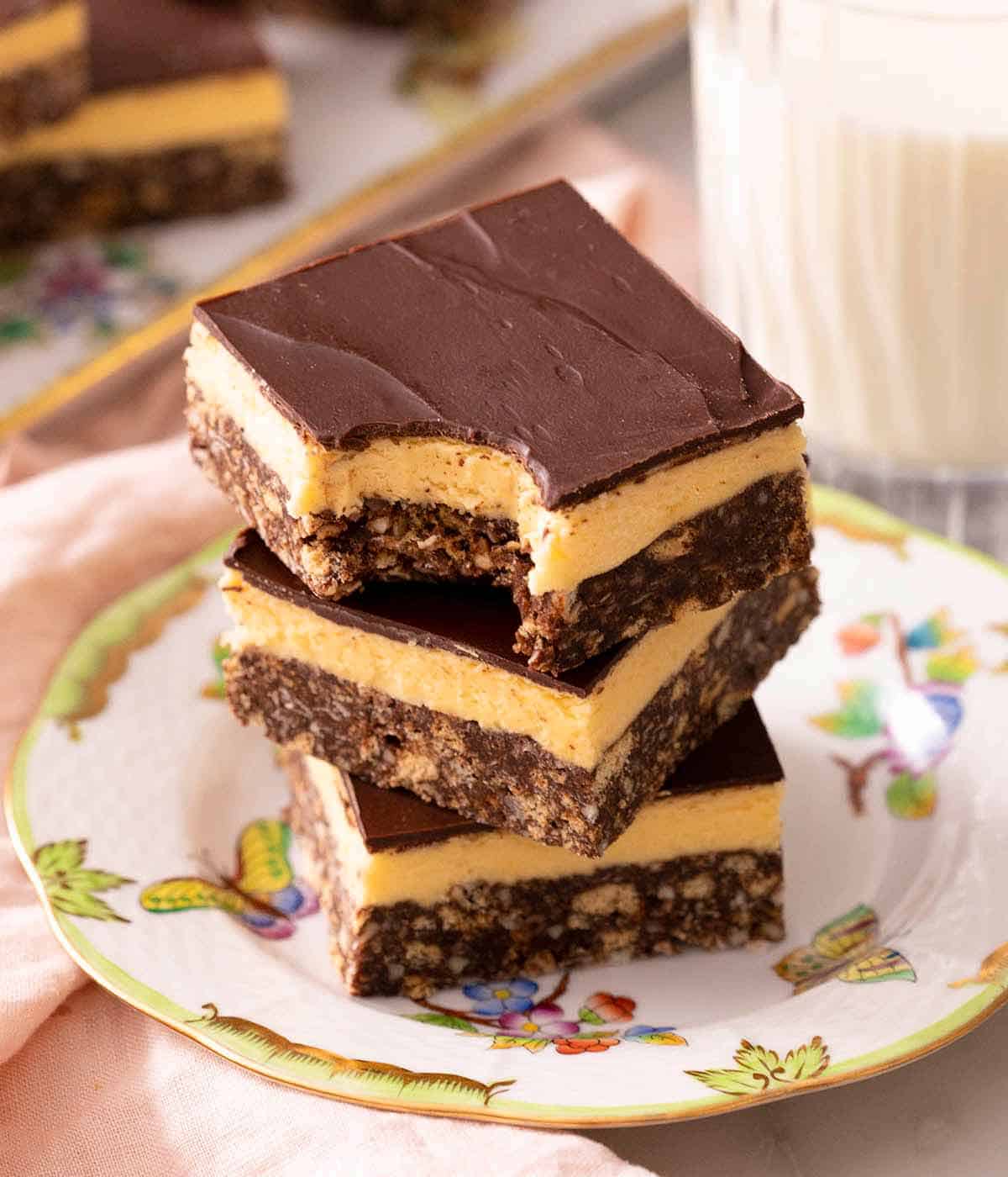 A stack of Nanaimo bars on a plate and one with a bite out