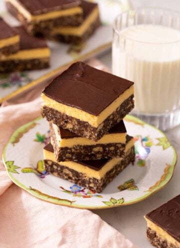 A stack of three Nanaimo bars on a plate. A glass of milk in the back.
