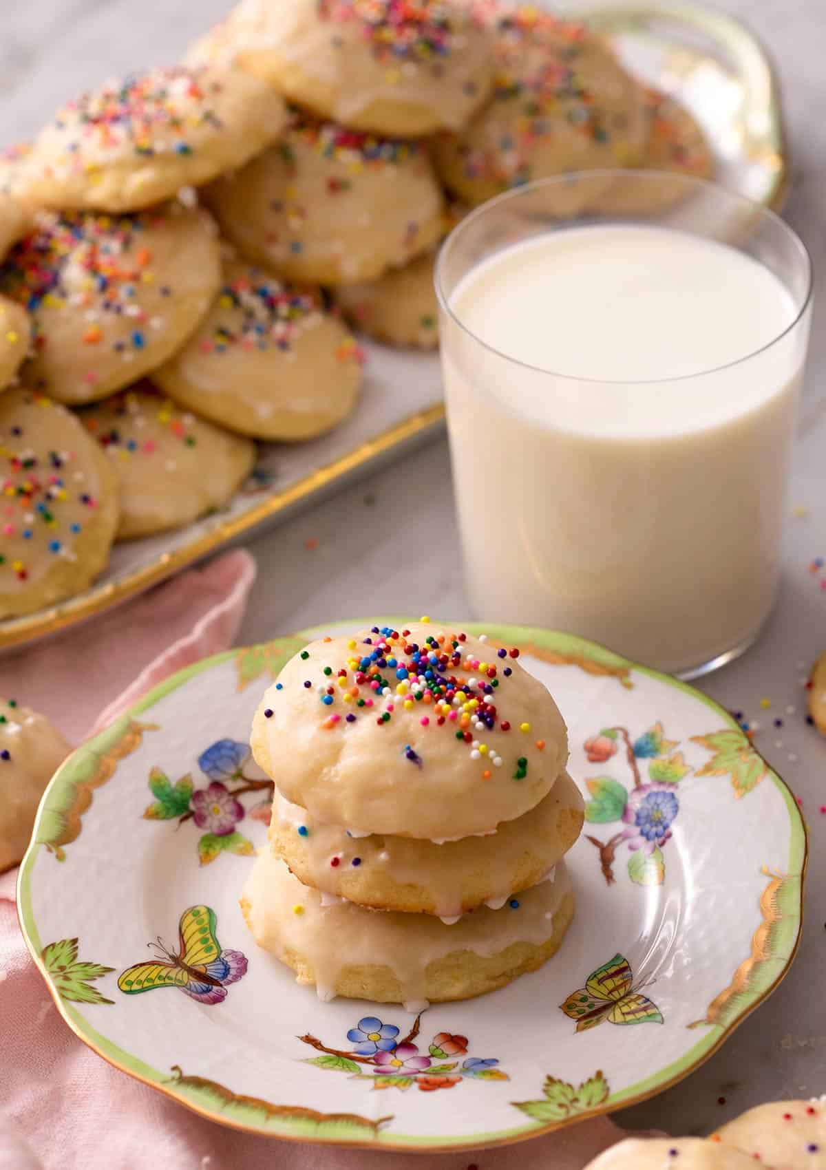 Ricotta cookies stacked on top of each other with a glass of milk in the background
