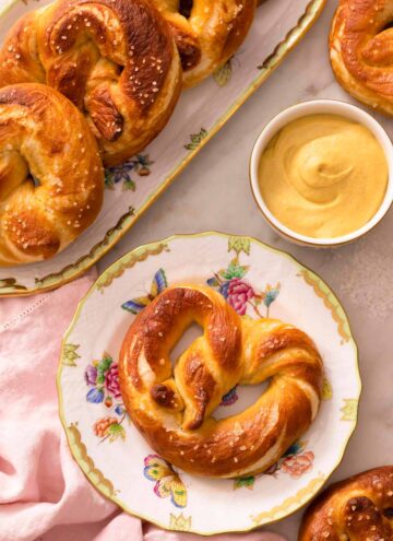 An overhead shot of a soft pretzel on a plate next to mustard