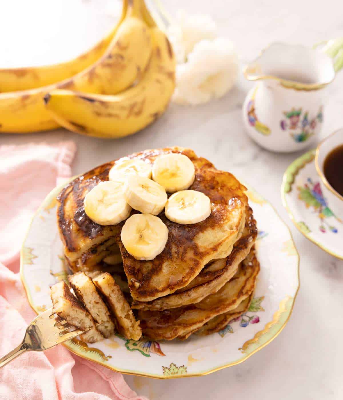 A stack of banana pancakes on a plate and some of a fork.