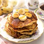 A stack of banana stacks with sliced bananas and maple syrup on top.