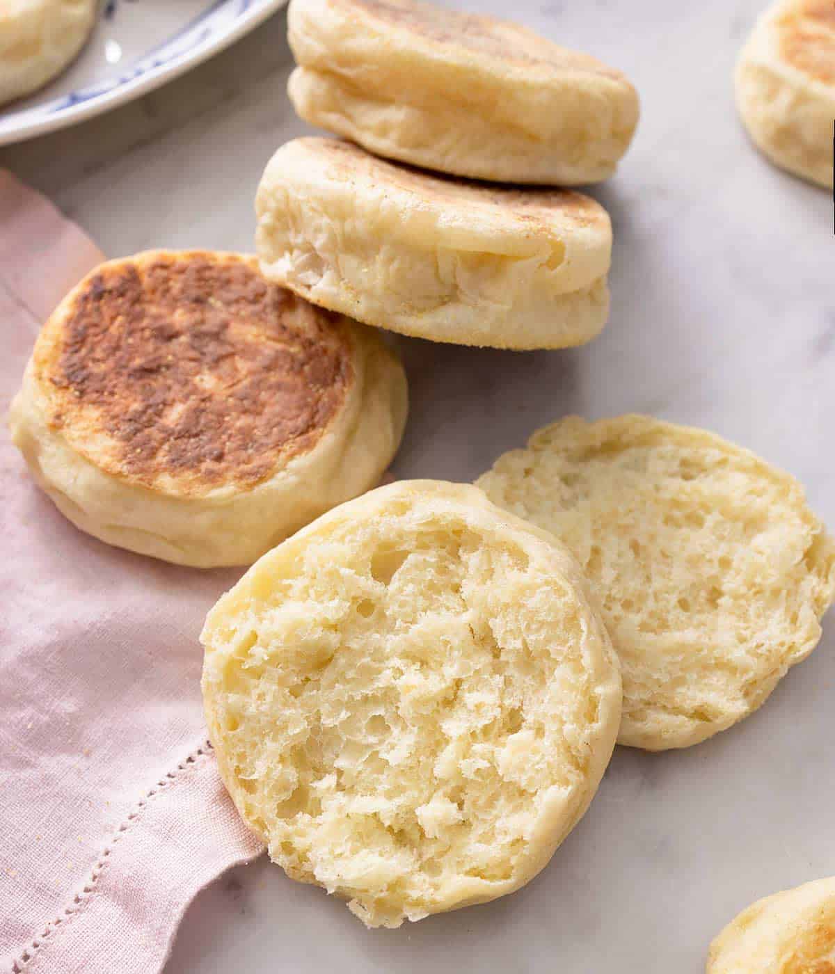 Some English muffins on a work surface and one cut in half.