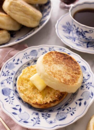 An English muffin cut in half and spread with butter on a plate.