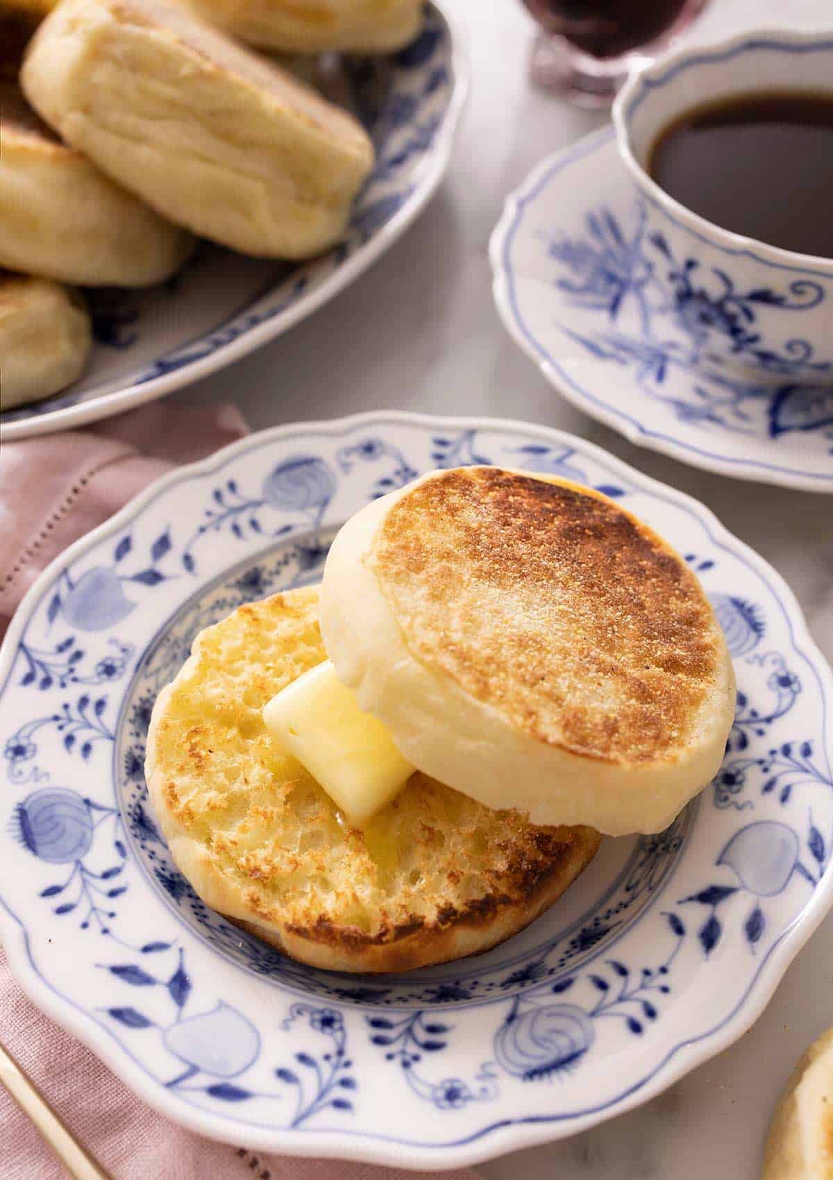 An English muffin cut in half and spread with butter on a plate.