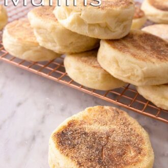 Pinterest graphic showing one English muffin in the foreground, with more piled on a wire rack behind it.