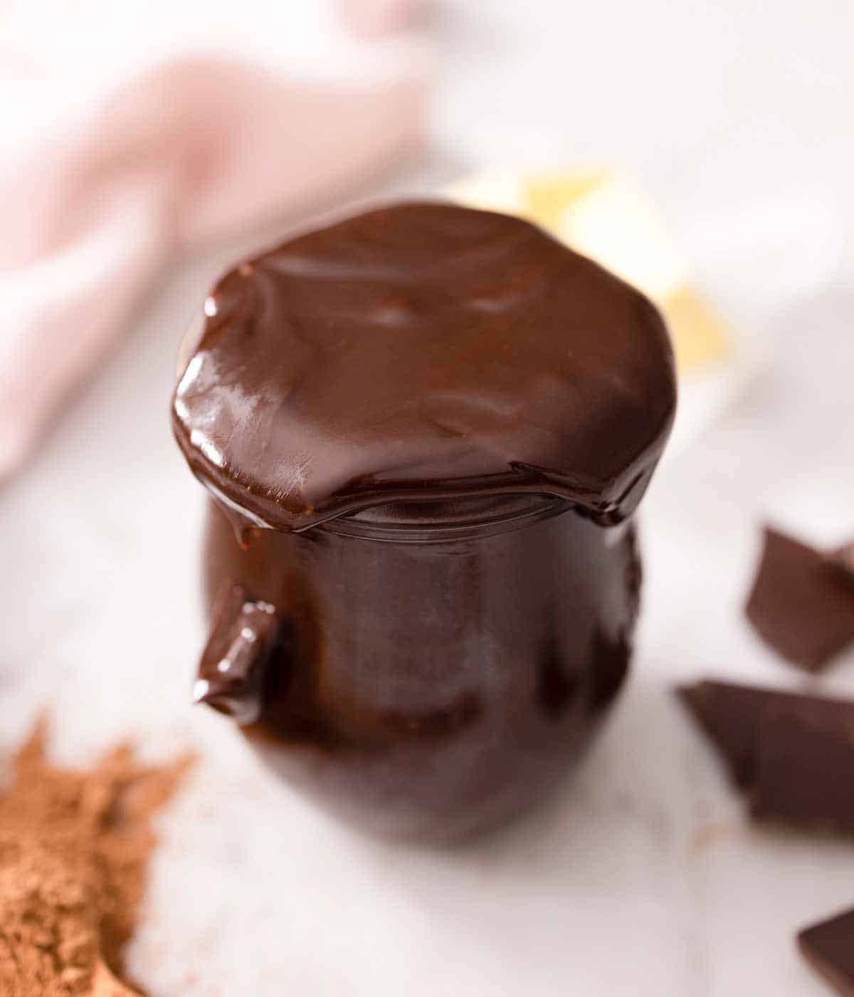 Hot fudge in a glass jar on a marble surface.