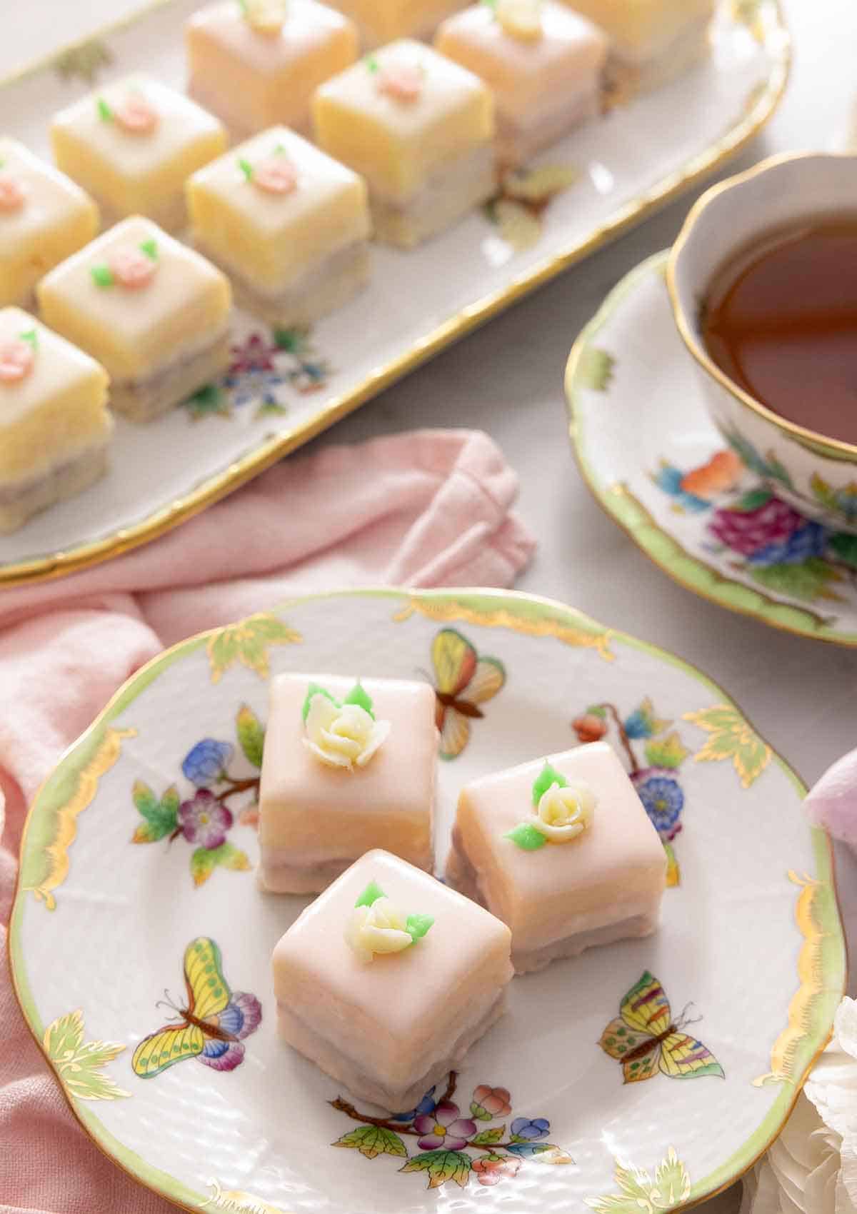 Overhead view of a serving platter of petit fours beside a plate with three.