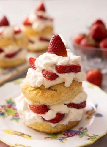 A close-up of an assembled strawberry shortcake with more out of focus in the background.