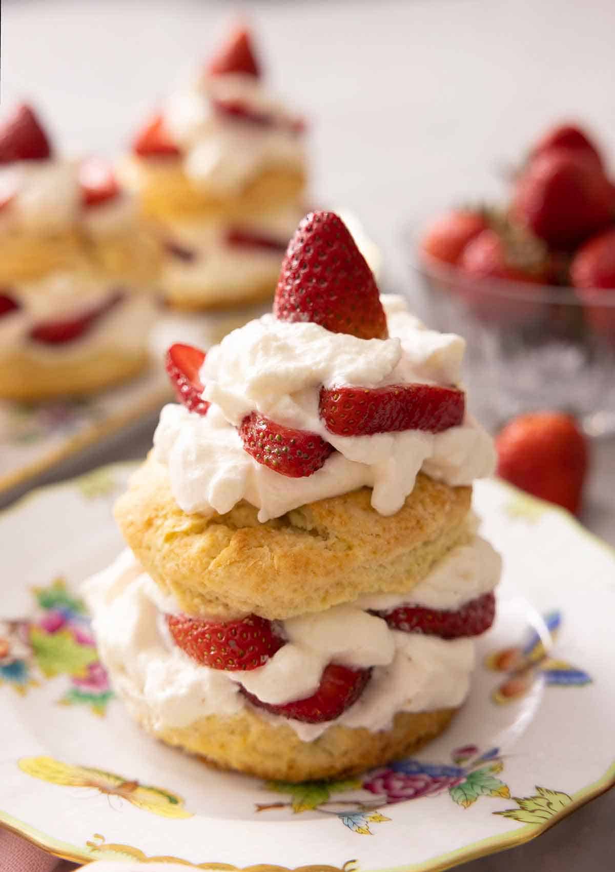 A close-up of an assembled strawberry shortcake with more out of focus in the background.
