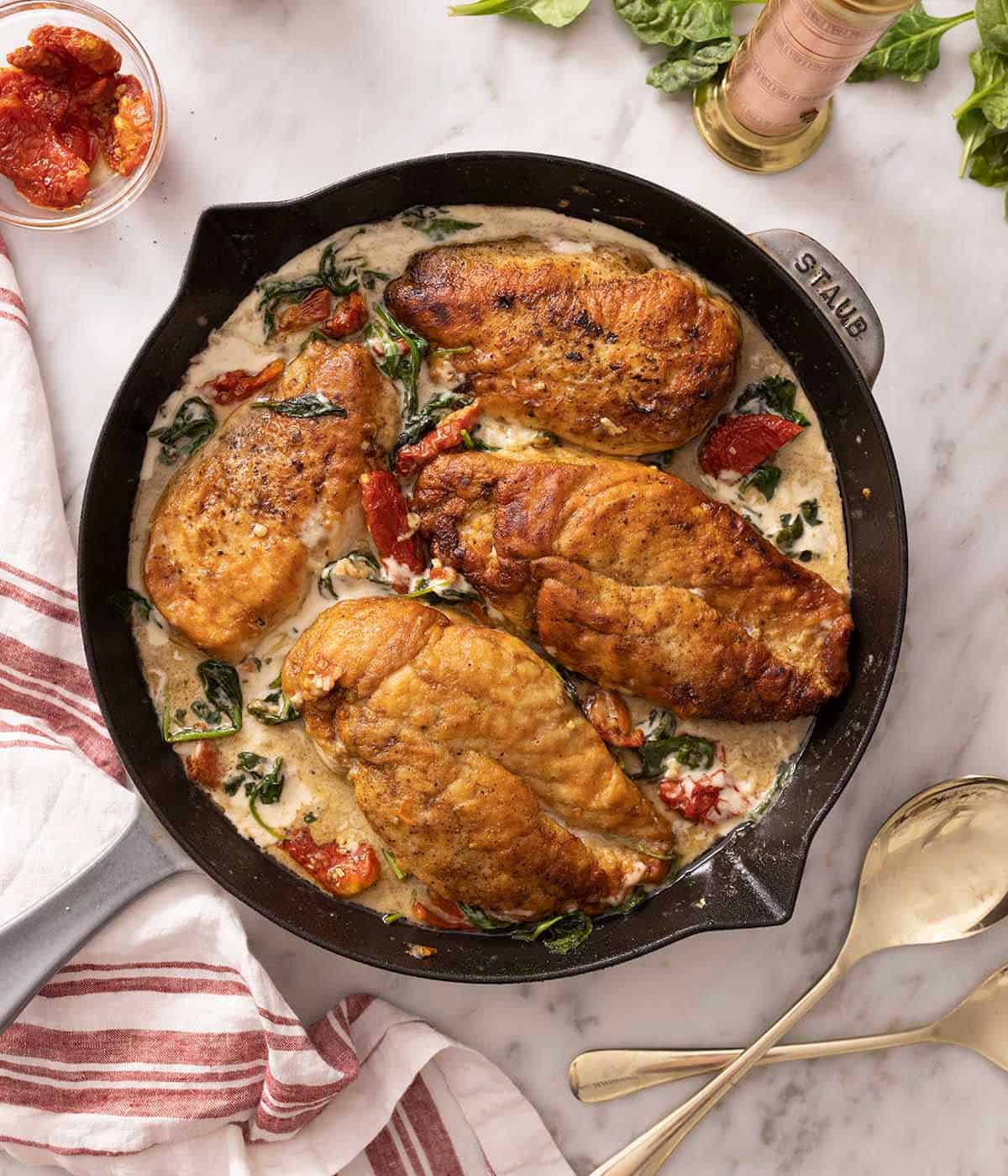 A grey Staub pan containing Tuscan chicken on a marble surface.