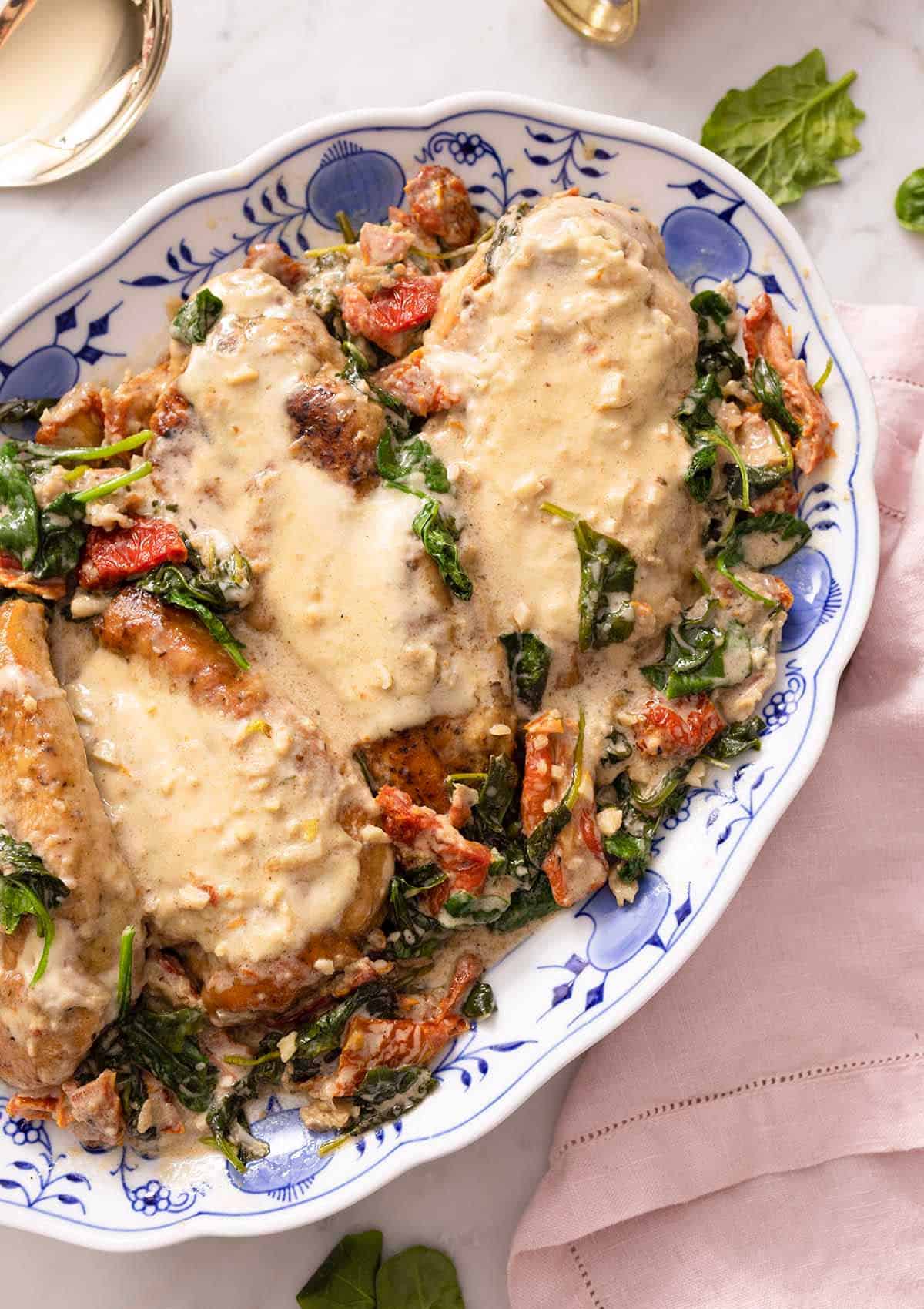 A white and blue floral platter with Tuscan chicken breasts with the sauce over top.