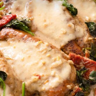 Pinterest graphic of a close up of two chicken breasts that are coated with a creamy Tuscan chicken sauce.