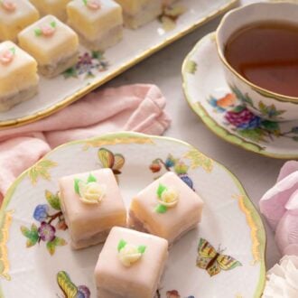 Pinterest graphic of three petit fours with small frosted flowers on top beside a cup of tea.
