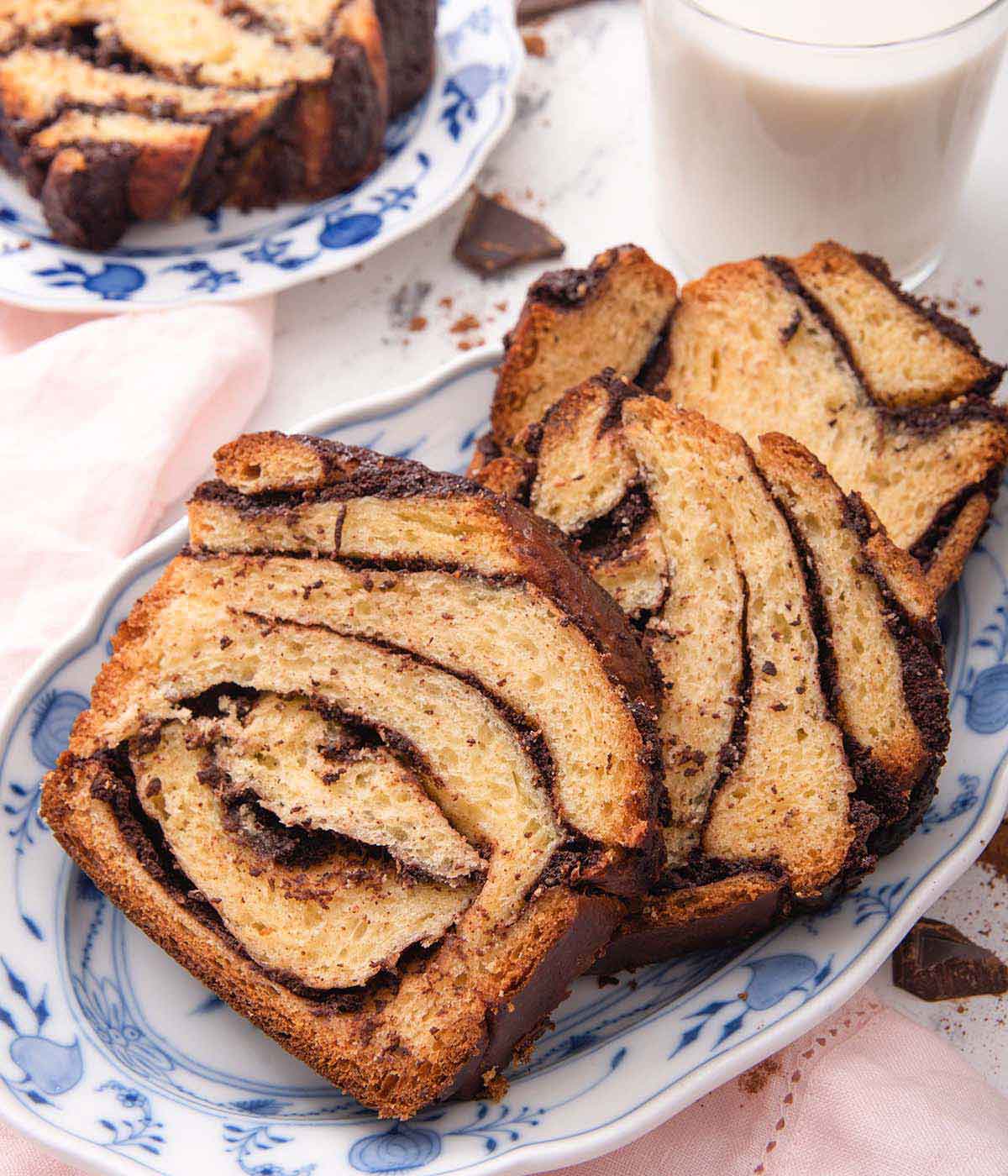 A blue and white platter with three slices of babka beside a glass of milk.