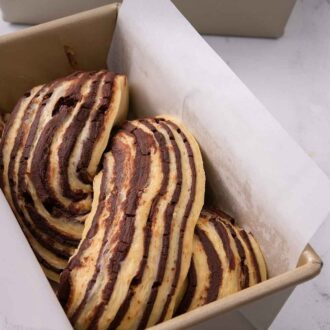 Pinterest graphic of a loaf pan lined with parchment paper with unbaked babka dough inside.